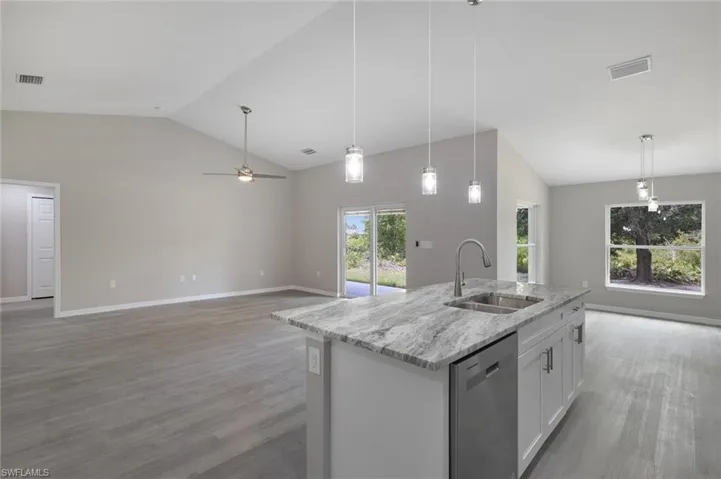 Kitchen with light hardwood / wood-style floors, dishwasher, a kitchen island with sink, light stone countertops, and white cabinets