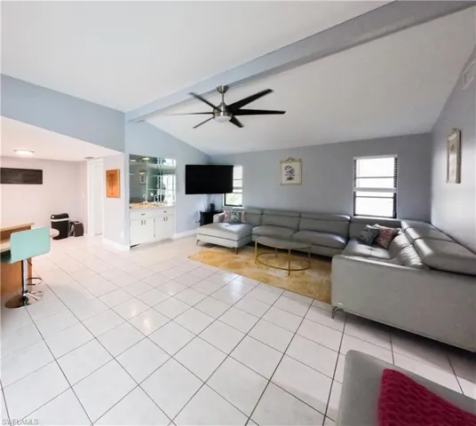 Tiled living room featuring vaulted ceiling with beams and ceiling fan