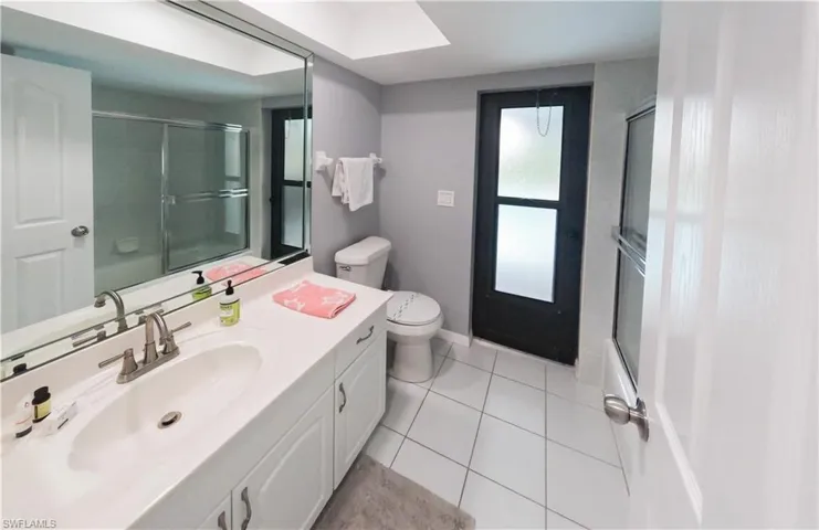 Full bathroom with enclosed tub / shower combo, tile patterned flooring, a skylight, toilet, and vanity