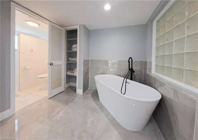 Bathroom with toilet, a bathing tub, tile patterned flooring, and tile walls