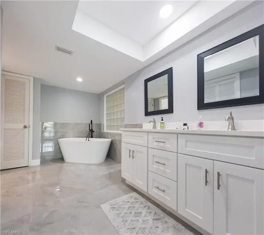Bathroom featuring tile patterned flooring, a washtub, double sink vanity, and tile walls
