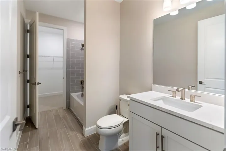 Ensuite bathroom with vanity, shower / bath combination, wood finish floors, and a walk in closet
