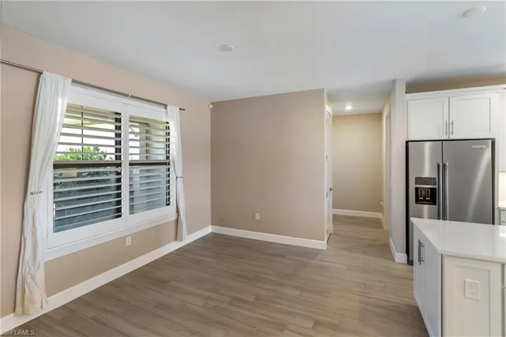 Kitchen with white cabinets, light wood-type tile flooring, stainless steel fridge with ice dispenser, light stone countertops, and recessed lighting