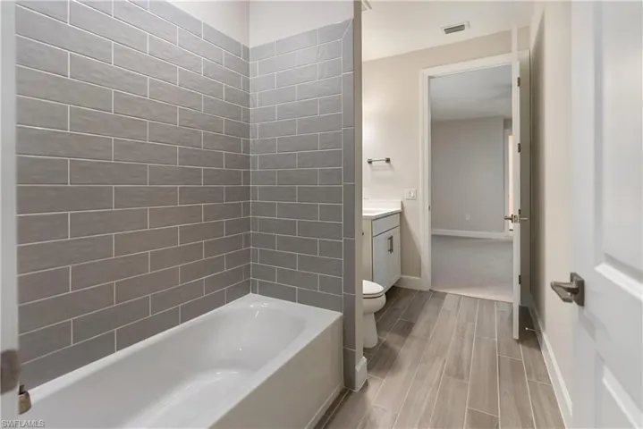 Ensuite bathroom with vanity, shower / bath combination, wood finish floors, and a walk in closet