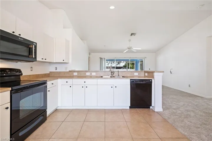 Kitchen with black appliances, light colored carpet, and white cabinetry