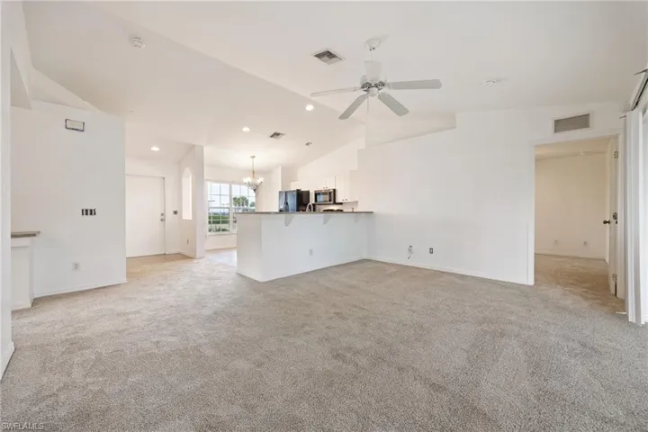 Unfurnished living room with light colored carpet, vaulted ceiling, a chandelier, ceiling fan, and recessed lighting