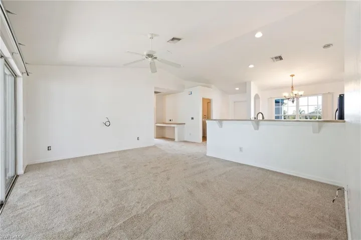 Unfurnished living room with vaulted ceiling, a chandelier, light colored carpet, a ceiling fan, and recessed lighting