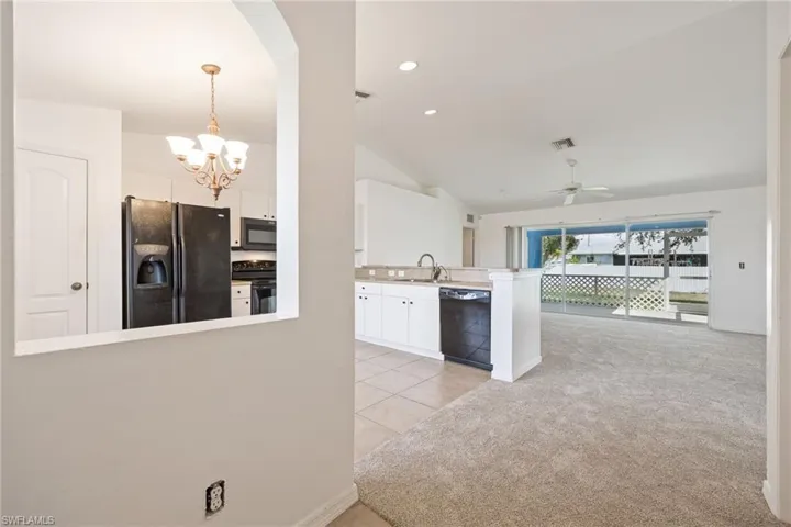 Kitchen with black appliances, white cabinetry, vaulted ceiling, light carpet, and pendant lighting