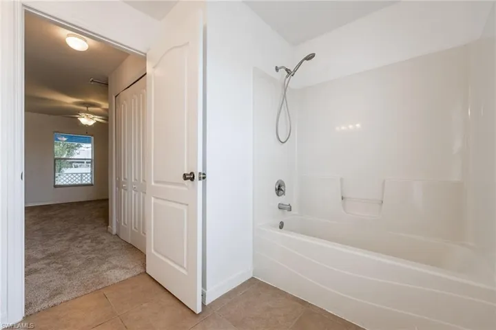 Full bathroom with light colored carpet, bathing tub / shower combination, a closet, light tile patterned flooring, and ceiling fan