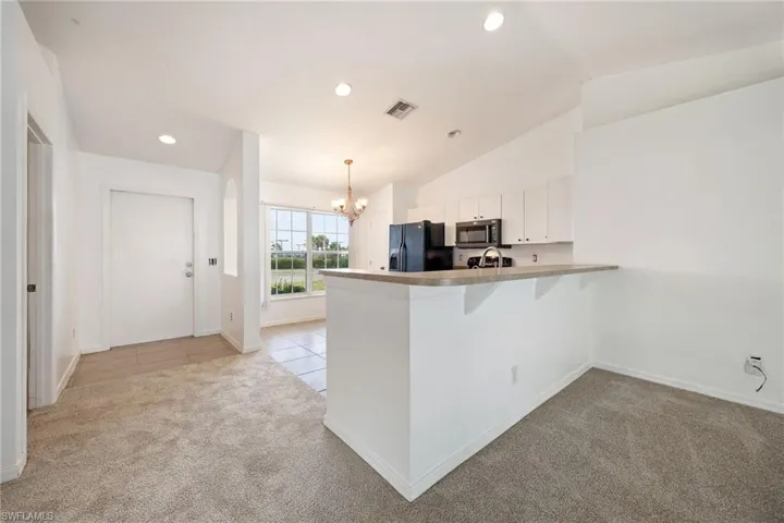 Kitchen featuring white cabinets, light colored carpet, recessed lighting, a chandelier, and black refrigerator with ice dispenser
