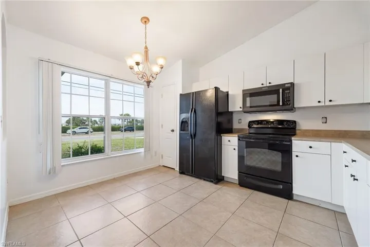 Kitchen with black appliances, white cabinets, vaulted ceiling, light countertops, and a chandelier