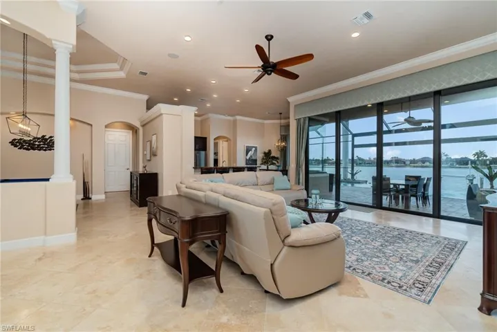 Living room with a water view, ornamental molding, ceiling fan, a wall of windows, and ornate columns