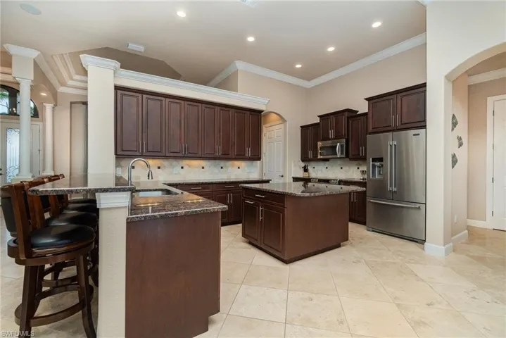 Kitchen with stainless steel appliances, kitchen peninsula, decorative columns, crown molding, and backsplash
