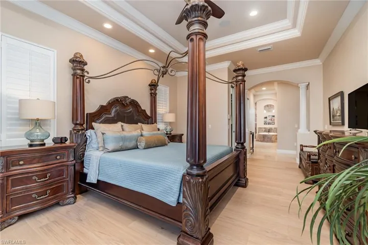 Bedroom featuring ornamental molding, ensuite bath, decorative columns, ceiling fan, and light hardwood / wood-style flooring