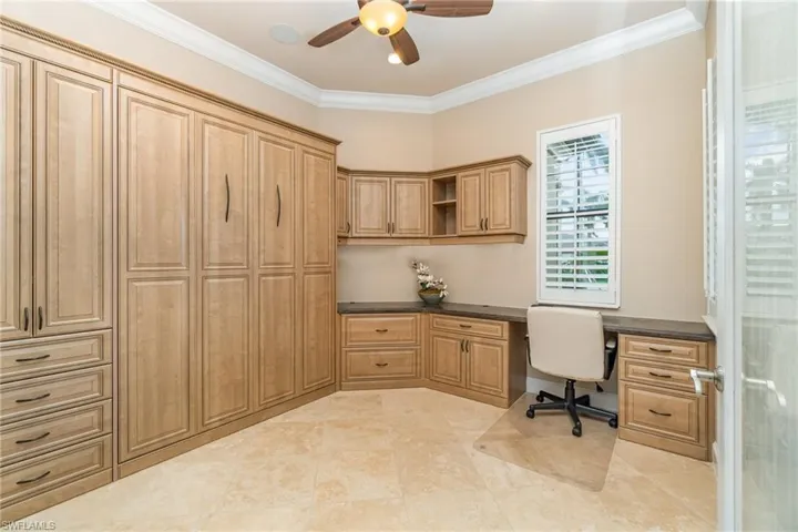 Unfurnished office with built in desk, ceiling fan, and crown molding