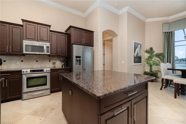 Kitchen featuring dark brown cabinets, dark stone countertops, appliances with stainless steel finishes, and ornamental molding