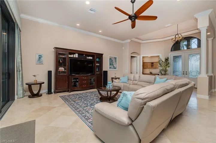 Living room with french doors, light tile patterned floors, decorative columns, ornamental molding, and ceiling fan