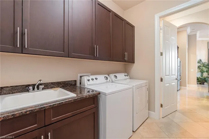 Laundry room featuring cabinets, sink, light tile patterned flooring, crown molding, and washer and dryer