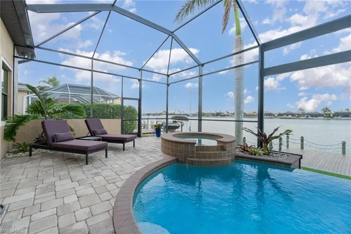 View of pool with a patio area, a water view, a lanai, and an in ground hot tub