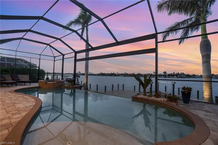 Pool at dusk with a patio area, a water view, a lanai, and an in ground hot tub