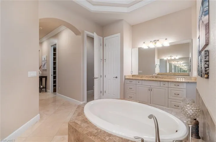 Bathroom featuring vanity, tile patterned floors, crown molding, and a relaxing tiled tub