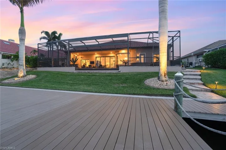 Back house at dusk featuring glass enclosure and a lawn
