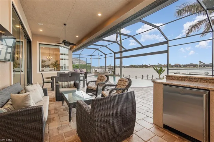 View of patio / terrace featuring glass enclosure, an outdoor kitchen, an outdoor living space, a water view, and ceiling fan