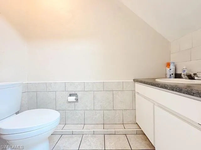 Half bath with tile walls, vanity, wainscoting, light tile patterned floors, and vaulted ceiling