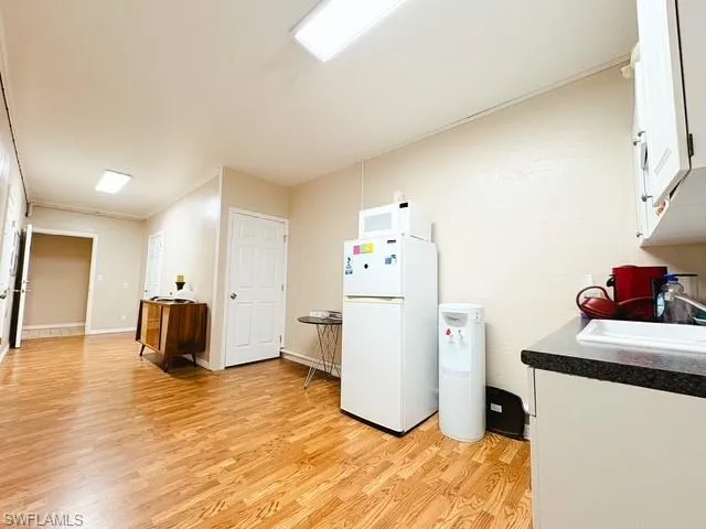Kitchen featuring white cabinetry, dark countertops, white appliances, and light wood-type flooring