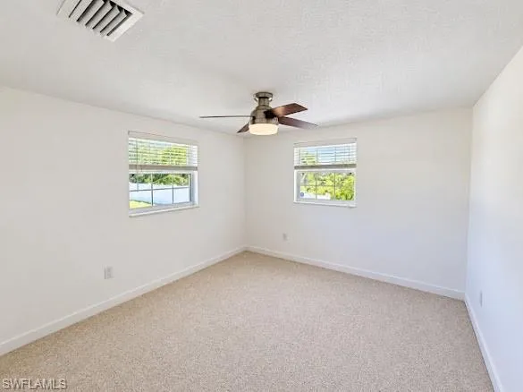 Neutral interior featuring light-toned wall-to-wall carpeting, dual windows with horizontal blinds, and a central ceiling fan with integrated lighting