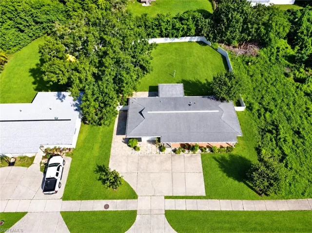 Aerial perspective featuring an expansive lawn, mature shade trees, a concrete driveway, and white perimeter fencing