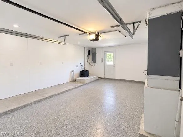 Garage interior featuring an epoxy-coated floor, recessed lighting, and a dedicated pedestrian access door