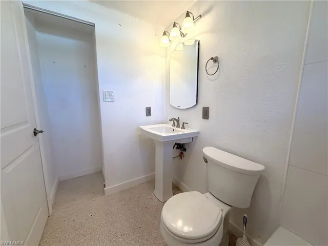 Pedestal sink with polished metal faucet, arched wall-mounted mirror, three-bulb vanity light fixture, and ceramic tile flooring