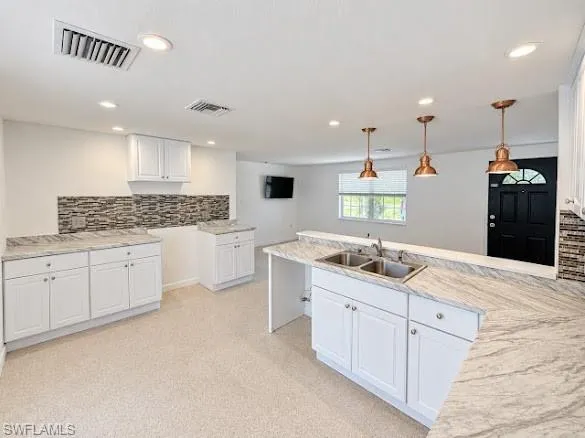 Kitchen featuring white shaker-style cabinetry, stone-patterned countertops, stacked-stone backsplash, recessed lighting, and metal pendant light fixtures