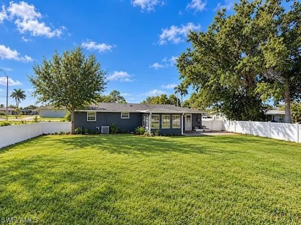 Expansive backyard featuring a manicured lawn, white vinyl fencing, mature trees, and a paved patio area
