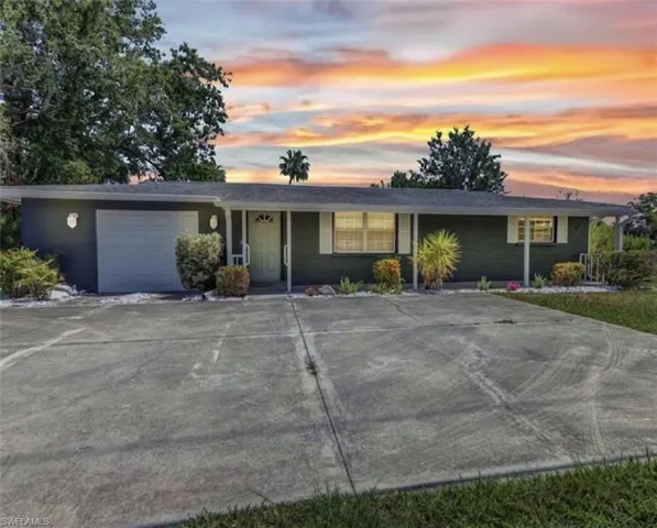Single-story ranch exterior featuring a painted brick facade, attached garage, covered front porch, and expansive concrete driveway