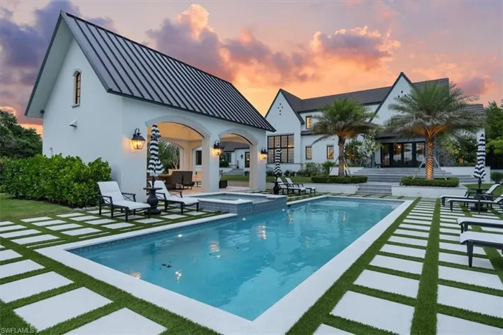 Pool at dusk with a patio area, a pool with connected hot tub, and an outbuilding