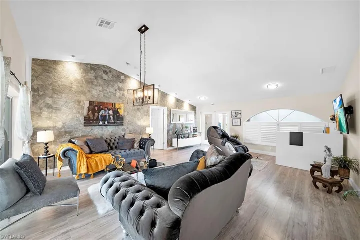 Living area featuring light wood finished floors, a chandelier, an accent wall, and high vaulted ceiling