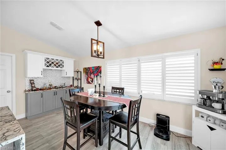Dining area with light wood finished floors, a chandelier, bar area, and lofted ceiling