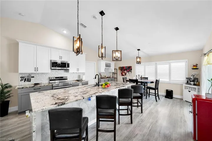 Kitchen featuring white cabinets, a breakfast bar, decorative backsplash, decorative light fixtures, and stainless steel appliances