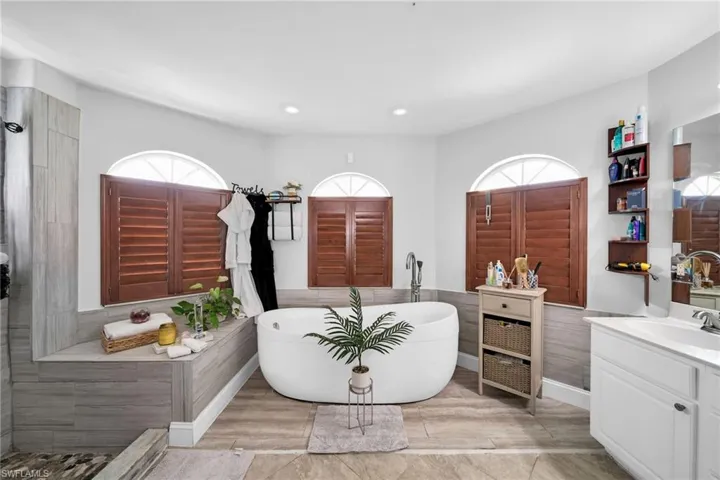 Bathroom featuring a soaking tub, vanity, wainscoting, recessed lighting, and light wood-style flooring
