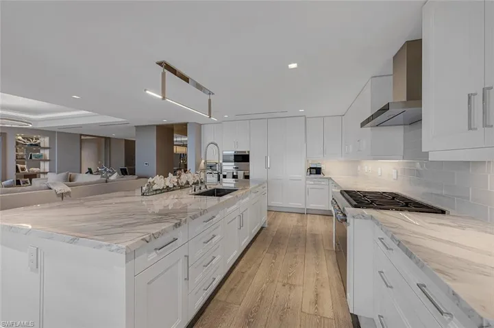 Kitchen featuring light hardwood / wood-style flooring, white cabinetry, sink, light stone countertops, and wall chimney range hood