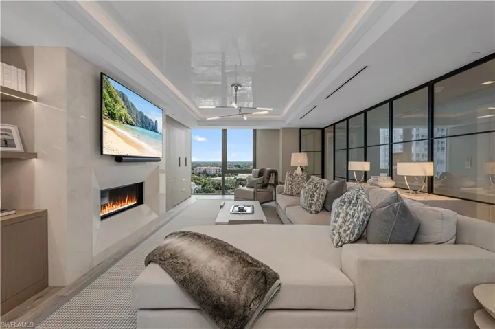 Living room featuring light hardwood / wood-style floors, a wall of windows, a tray ceiling, and ceiling fan