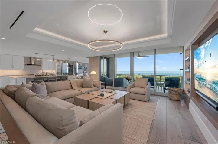 Living room with a raised ceiling, a wall of windows, ceiling fan, and light wood-type flooring