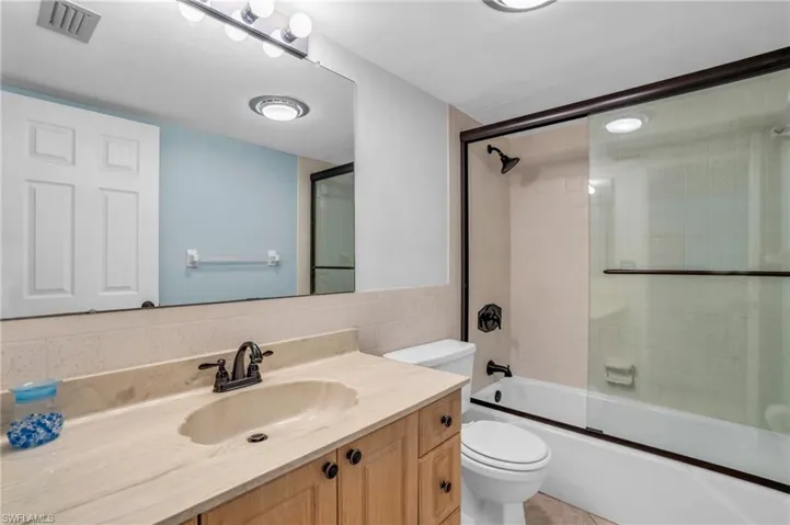 Full guest bathroom featuring tile walls, backsplash, combined bath / shower with glass door, and toilet
