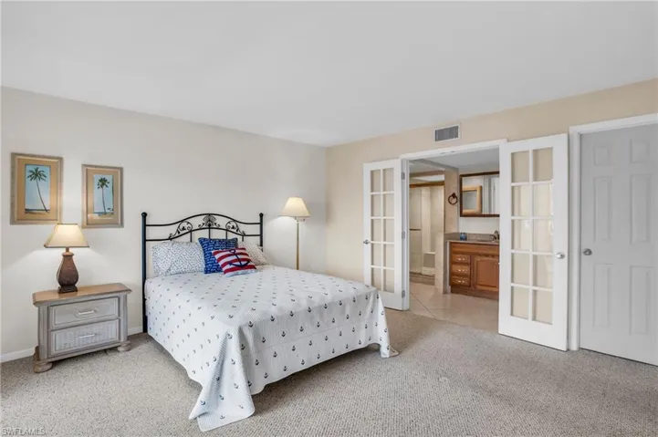 Bedroom featuring french doors, ensuite bathroom, and light colored carpet
