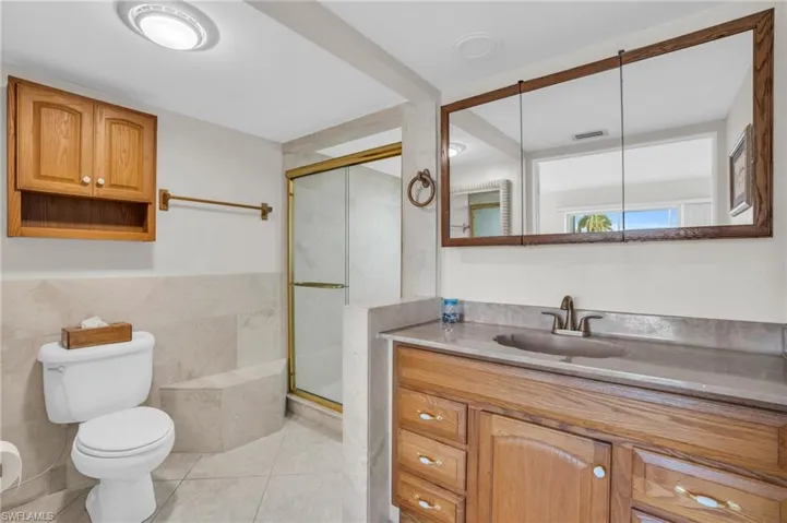 Bathroom with tile walls, toilet, tile flooring, a shower with door, and vanity
