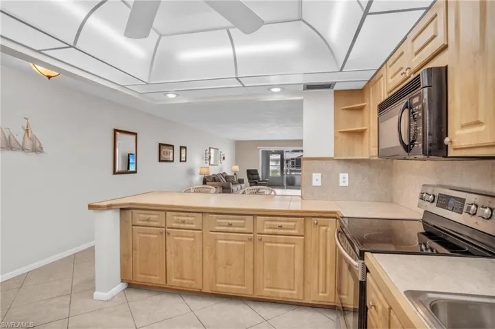 Kitchen with light brown cabinetry, backsplash, ceiling fan, electric range, and light tile floors