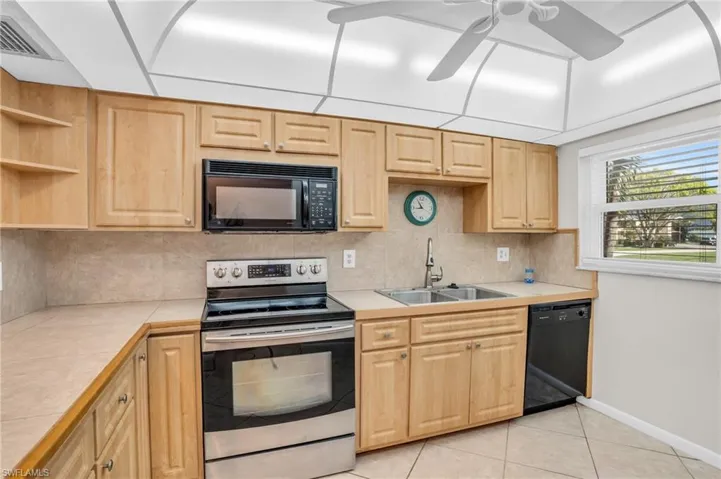 Kitchen with ceiling fan, black appliances, tile countertops, sink, and light tile floors