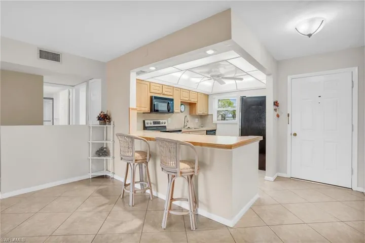 Kitchen featuring black appliances, kitchen peninsula, backsplash, a breakfast bar, and ceiling fan